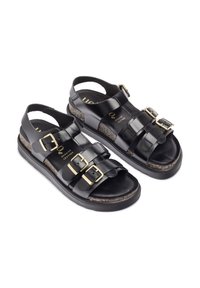 Zwarte leren sandalen met drie gespsluitingen, gestructureerde kurken tussenzool en platte rubberen buitenzool. Gouden hardware accenten zichtbaar.