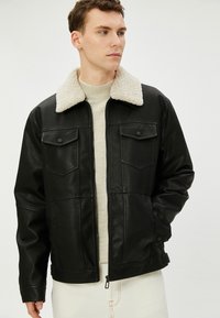Zwarte leren jas met een beige schapenvacht kraag, twee borstzakken en een ritsontsluiting. Gestructureerde afwerking en lange mouwen.