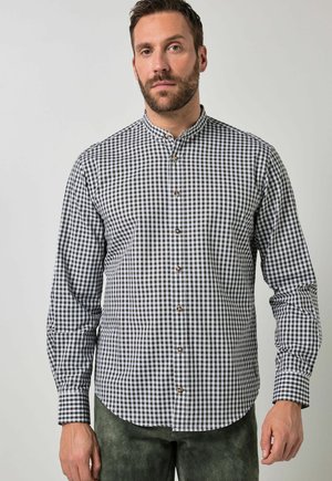 Mann trägt ein langärmeliges schwarz-weiß kariertes Hemd mit Stehkragen vor schlichtem Hintergrund.