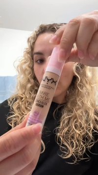 NYX Bear With Me Concealer Serum i ett klart rör med ett rosa lock, som har en pipett-topp och en ljusbeige vätska inuti.