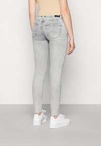 Jeans skinny de denim gris con una cintura de media altura, dos bolsillos traseros y un ligero desvanecimiento. Combinados con zapatillas blancas y una blusa beige.
