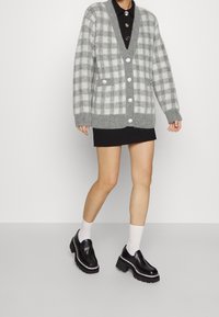 Grå rutigt stickad cardigan med djup V-ringning, knäppning framtill och två fickor. Kombineras med en svart minikjol och plattformsskor.