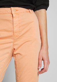 Persikofärgade bomullschinos med en slät textur, framdragkedja och knappstängning. Har diskreta sömmar längs fickorna.