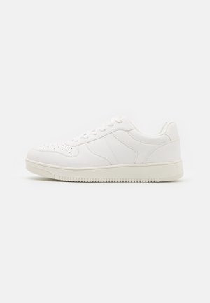 Witte lage sneaker met veters en een geperforeerde neus, van opzij getoond op een effen lichte achtergrond.