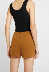 Top corto negro con encaje combinado con pantalones cortos de ante marrón de talle alto. La tela parece suave con una textura lisa.