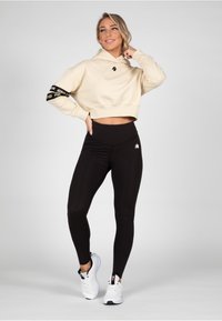 Felpa beige tagliata con logo nero e dettagli sulle maniche, abbinata a leggings neri a vita alta con un piccolo logo sulla coscia.