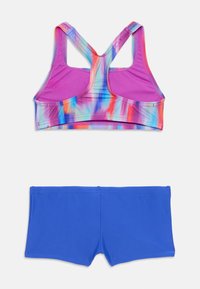 Športni modrček z večbarvnim tie-dye vzorcem v roza, modri in oranžni barvi; kombiniran z enobarvnimi modrimi kratkimi hlačami. Obe sta narejeni iz gladkega, raztegljivega materiala.