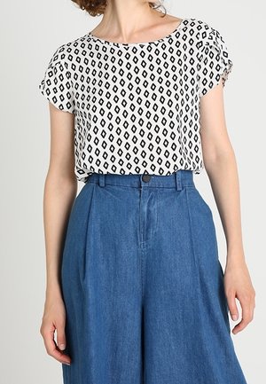 Witte blouse met korte mouwen en zwart ruitpatroon, ingeruild in een high-waisted wijde blauwe spijkerbroek.