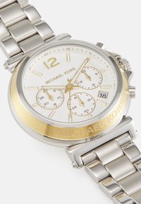 Orologio in acciaio inox con finiture in argento e oro e quadrante bianco. Presenta sottoquadranti cronografici, visualizzazione della data e un bracciale a maglie.