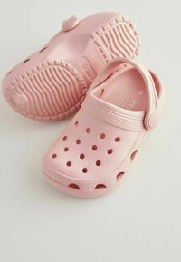 Zuecos de plástico rosa con orificios de ventilación, una suela texturizada y una correa ajustable para un ajuste seguro. Diseño ligero para mayor comodidad.