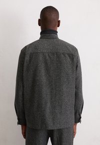 Grau strukturierte Jacke mit kragenumschlag, sichtbaren Nahtdetails und Knopfmanschetten. Der Stoff hat ein dezentes gepunktetes Muster.