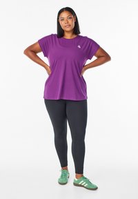 Lila Kurzarm-T-Shirt mit runder Ausschnitt, kombiniert mit schwarzen Leggings und grünen Sneakers mit weißen Streifen. Glattes Material, lässige Passform.