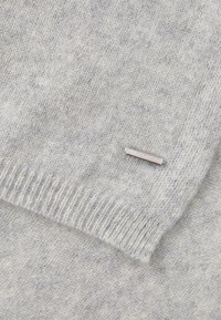 Tissu tricoté gris clair avec un bord côtelé et une petite étiquette rectangulaire en métal argenté attachée près du pli.