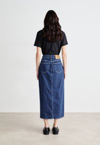 Jupe maxi en jean bleu foncé avec une coupe droite, cinq poches et une étiquette en cuir de marque à l'arrière ; associée à un t-shirt noir.