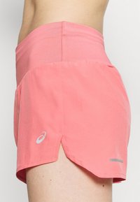 Vaaleanpunaiset urheilushortsit, joissa on istuva vyötärö, leveä lahje, heijastavat yksityiskohdat ja sivuhiat helpottamassa liikkumista.