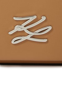 Kožni proizvodi u boji tan s srebrnim logotipom u tečnom script dizajnu, s glatkom teksturom i elegantnim, minimalističkim izgledom.