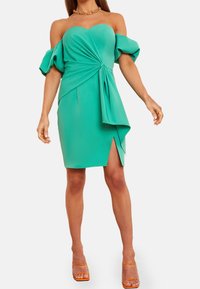 Turkusowa sukienka na jedno ramię z bufiastymi rękawami, zawiązywana, z wysokim rozcięciem po boku. Wykonana z elastycznego materiału.