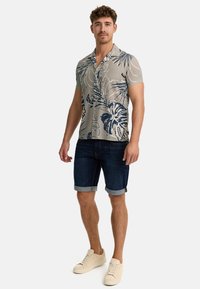 Camisa de manga corta de color gris claro con un patrón floral azul, combinada con pantalones cortos de mezclilla oscura y zapatillas en color crema.
