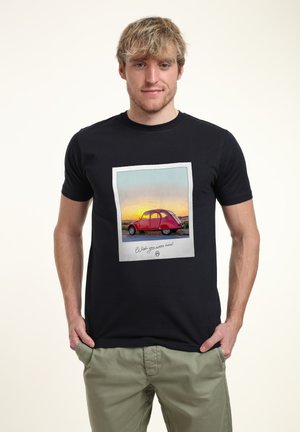 Sort t-shirt med et trykt vintage billede af en rød bil inden for en hvid ramme. Designet inkluderer en solnedgangsbagtgrund og håndskrevet tekst.