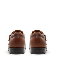 Zapatos de cuero marrón con un diseño elegante, punta redondeada y un tacón bajo. Con tira en la parte trasera y un detalle de costura sutil.