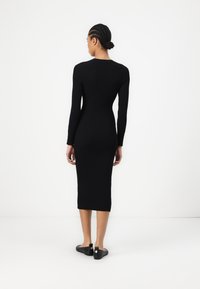 Robe midi noire côtelée avec des manches longues et une coupe ajustée. Dotée d'un col rond et de détails minimalistes, accompagnée de ballerines noires.