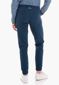 Pantalones tapered azul marino con puños elásticos, dos bolsillos traseros y cintura con presilla, combinados con zapatillas blancas.