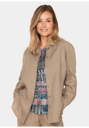 Beige Leinenhemd mit Knöpfen über einem mehrfarbigen Top mit verschiedenen geometrischen Mustern. Textur aus Naturfasern, lässige Passform.