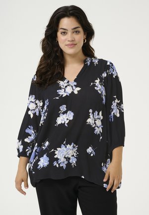 Blouse noire à motifs floraux bleus et blancs, tissu doux, manches 3/4 et design en V. Coupe ample avec un ourlet arrondi.