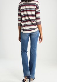 Striped long-sleeve top in cream, red, and navy, paired with blue slim-fit jeans. Notable features include three-quarter sleeves and a relaxed fit.