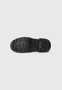 Čierna robustná podrážka topánky s hlbokým vzorom a logom Timberland umiestneným na strede, zobrazená na hladkom bielom pozadí.