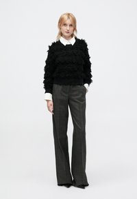 Black textured sweater with ruffled fabric, paired with gray plaid wide-leg trousers. White collared shirt visible underneath.