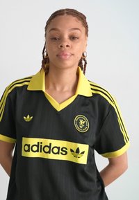 Melna futbola krekla ar dzelteniem akcentiem, ar apkakli, horizontālām svītrām un logotipa detaļām. Izgatavots no gludas, elpojošas auduma.