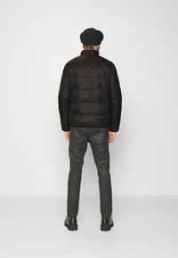 Svart puffjacka med horisontella quiltade sektioner, i kombination med slim-fit svarta läderbyxor och svarta skor. Utsikt bakifrån.