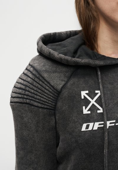 Σκούφο με καφέ γκρι χρώμα, με υφασμένα ριμπ λεπτομέρειες στους ώμους και λευκό λογότυπο με διασταυρωμένα βέλη και το κείμενο "OFF-" στο στήθος, φορεμένο από ένα άτομο.
