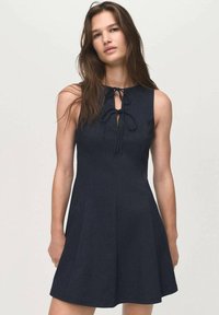 Marineblauwe denimjurk met een aansluitende bodice, een uitlopende rok en een striksluiting bij de halslijn. Soepele textuur en mouwloos ontwerp.