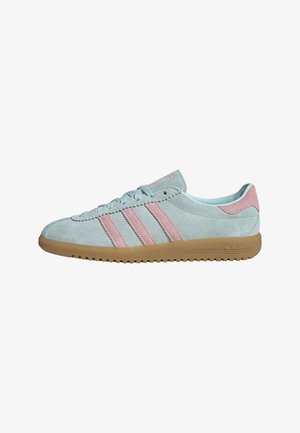 Zapatilla deportiva de ante azul claro con rayas rosas, lengüeta trasera rosa, cordones frontales y suela de goma, vista lateral sobre fondo blanco.
