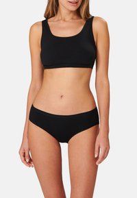 Bralette sportivo nero, senza cuciture, con una fascia ampia e scollo a barca. Abbinato a slip neri a vita bassa con una fascia in vita liscia.
