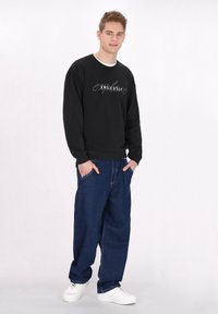 Hanorac negru cu grafică „ENDLESSLY”, asortat cu pantaloni din denim albastri largi și adidași albi. Design simplu și casual.