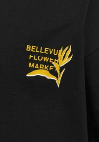 Juodas medvilnės marškinėliai su geltonai siuvinėtu tekstu "BELLEVUE FLOWER MARKET" ir dekoratyvine augalų motyvu.