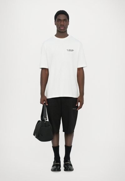 T-shirt blanc à manches courtes avec texte noir, shorts cargo noirs, sac noir, chaussettes noires et chaussures noires. Design simple et moderne.
