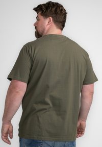 Camiseta de algodón verde oliva con mangas cortas, cuello redondo y un ajuste relajado. Costuras visibles y una etiqueta en el dobladillo.