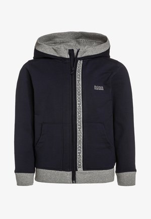 Granatowa bluza z kapturem wykonana z miękkiego materiału, z szarym podszyciem kaptura, zamkiem na przodzie z taśmą z logo oraz ściągaczami na mankietach i u dołu.