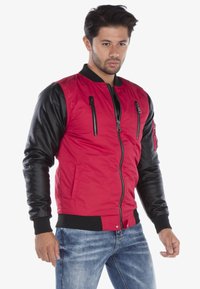 Rode bomberjack met zwarte leren mouwen, ritszakken aan de voorkant, ribbelkraag en -manchetten, en een aansluitende tailleband.