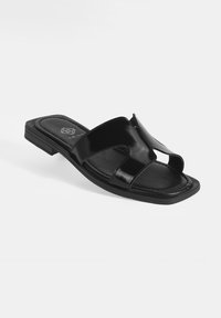 Zwarte slidesandalen met een glanzende afwerking. Twee brede banden hebben uitsparingen. Gevoerde voetbed en een lage rubberen zool.