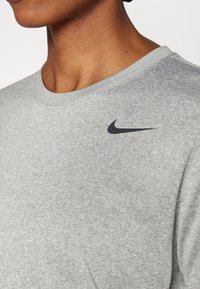Hallhallane puuvillane dressipluus, millel on ümmargune kaelus, pehme tekstuur ja väike must Nike logo vasakul ülanurgas.