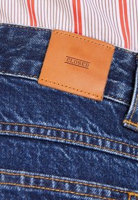 Jeans i denim med blå finish, utrustade med en brun läderetikett märkt "CLOSED" och orange sömmar på fickor och sömmar.