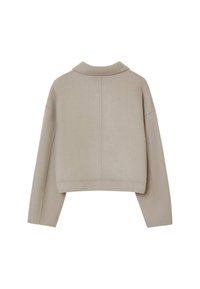 Veste courte beige avec une texture douce, un col tailleur et des épaules tombantes. Présente un dos épuré sans matériel visible.