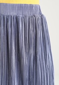 Gonna midi plissettata in tessuto azzurro chiaro testurizzato. Presenta una cintura larga e pieghe verticali per una silhouette fluida.