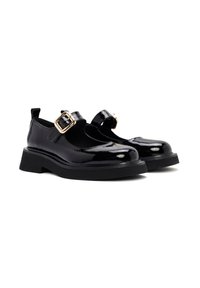 Zapatos de charol negro con punta redonda, suela de plataforma plana y tira al tobillo con un detalle de hebilla dorada. Superficie lisa y brillante.