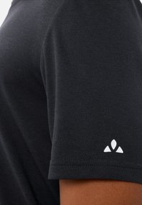 Zwart t-shirt met korte mouwen, gemaakt van textuurstof, met een klein wit logo op de linker mouw en gestikte details.